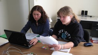 Finella working on laptop while Elspeth reads legal papers